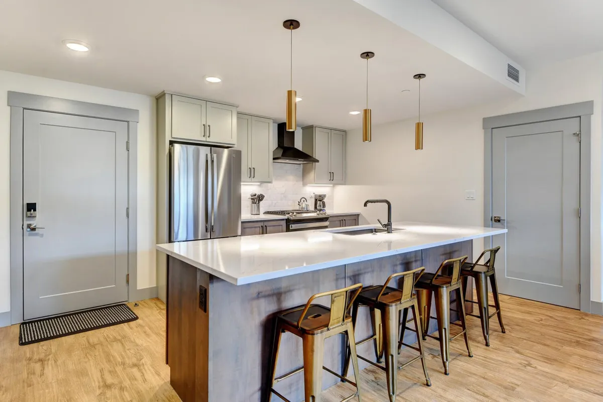 A modern kitchen with a central island, gleaming stainless steel appliances, and pendant lights casting a warm glow. The layout is inviting for both cooking and casual dining, emphasizing an open, communal feel.