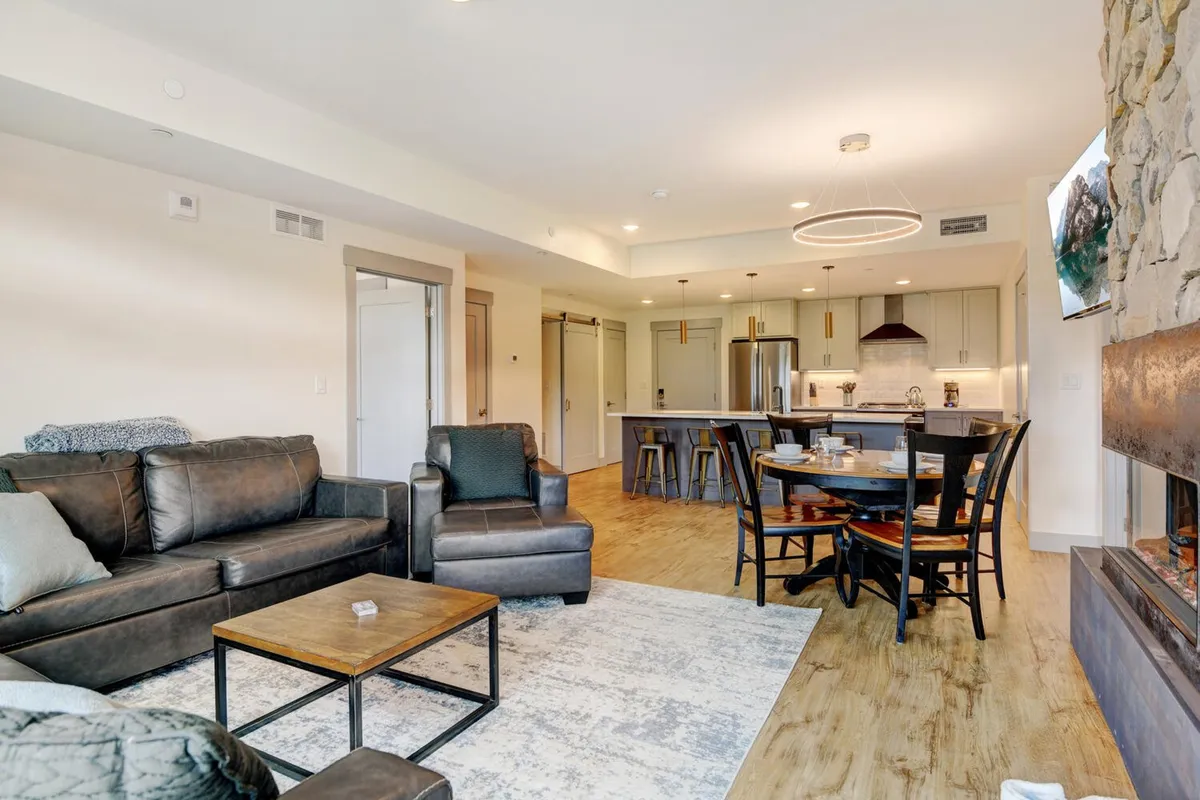 A welcoming, open-concept interior with a comfortable leather sofa, spacious dining table, modern kitchen island, and a cozy fireplace. The space is designed for socializing, entertaining friends, and relaxing together after a day of adventure.