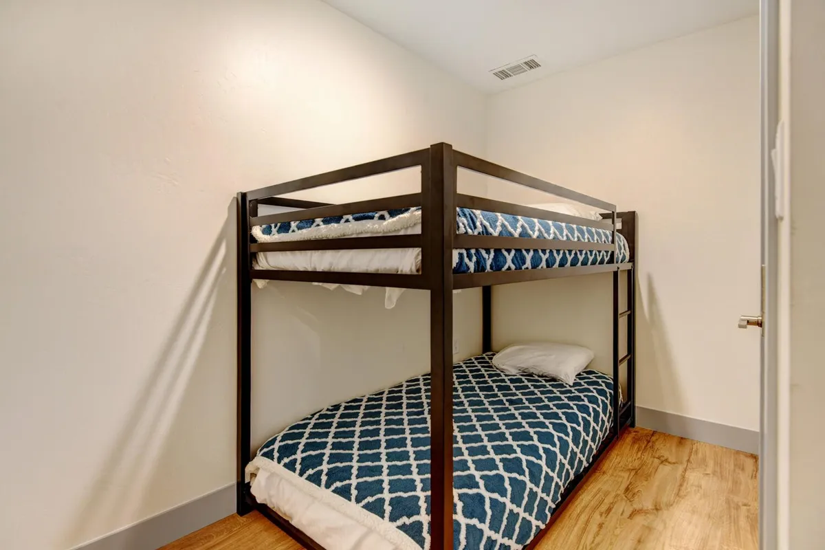 A cozy bunk nook with a compact bunk bed dressed in playful bedding, inviting for both children and adults. The space suggests comfort, late-night conversations, and a flexible sleeping arrangement for families or groups.