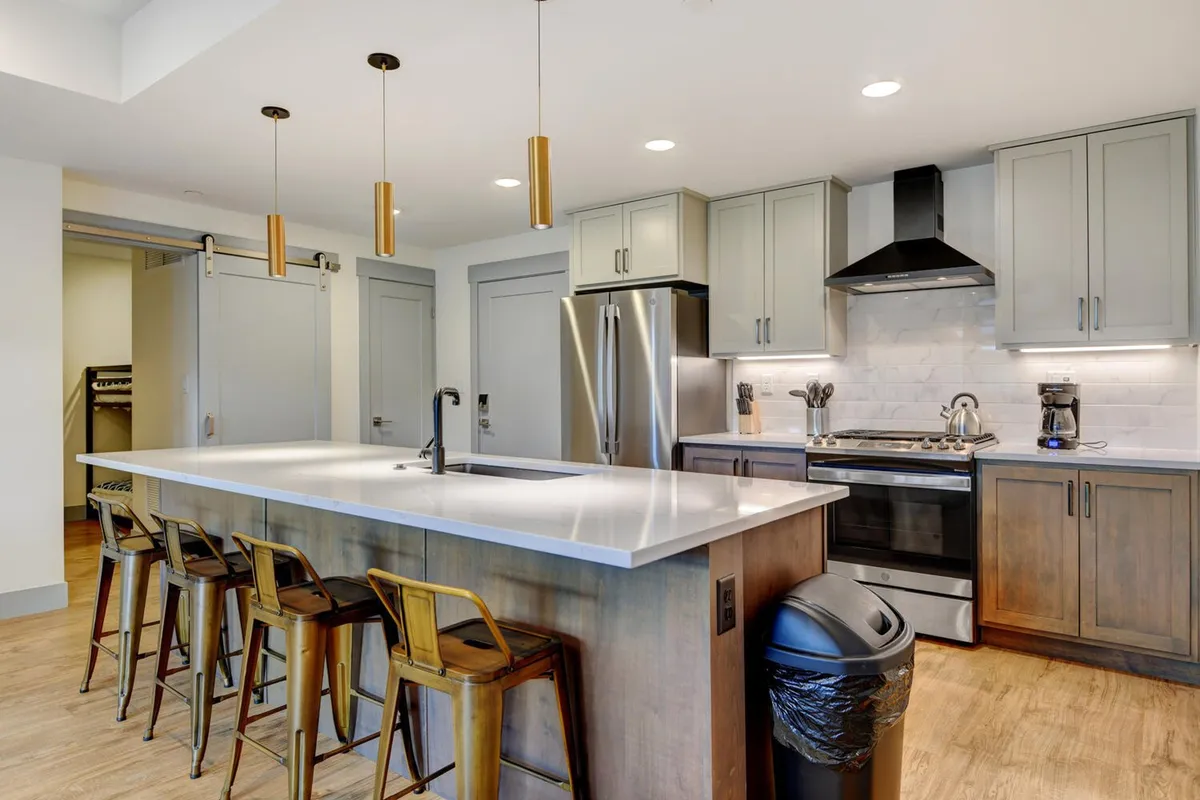 The hero image showcases a bright, contemporary kitchen featuring a spacious island with stylish pendant lighting above, gleaming stainless steel appliances, and ample seating—inviting spaces perfect for gathering, cooking, and sharing memorable moments.
